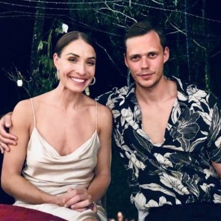 Bill Skarsgård and Alida Morberg are sitting by the table posing for the picture.